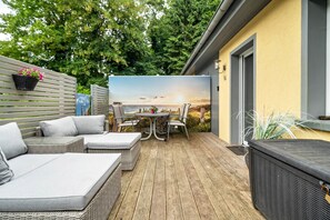 Una terraza de madera con mobiliario exterior, una mesa y sillas.