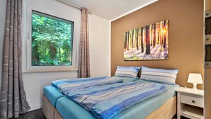 Ein Schlafzimmer mit einem Bett, einem Nachttisch, einem Fenster mit Vorhängen und einem Bild an der Wand.