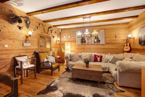 L’intérieur d’une cabane en rondins, avec un plancher en bois, un canapé, des fauteuils, une table basse et des têtes d’animaux fixées au mur.