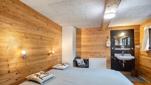 Una habitación con paneles de madera, una cama, una silla, un radiador y un baño con lavabo y espejo.