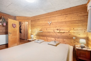 Une pièce aux murs lambrés, avec un lit, deux tables de chevet dotées de lampes, une décoration en forme de cœur et une tête de cerf accrochée au mur.