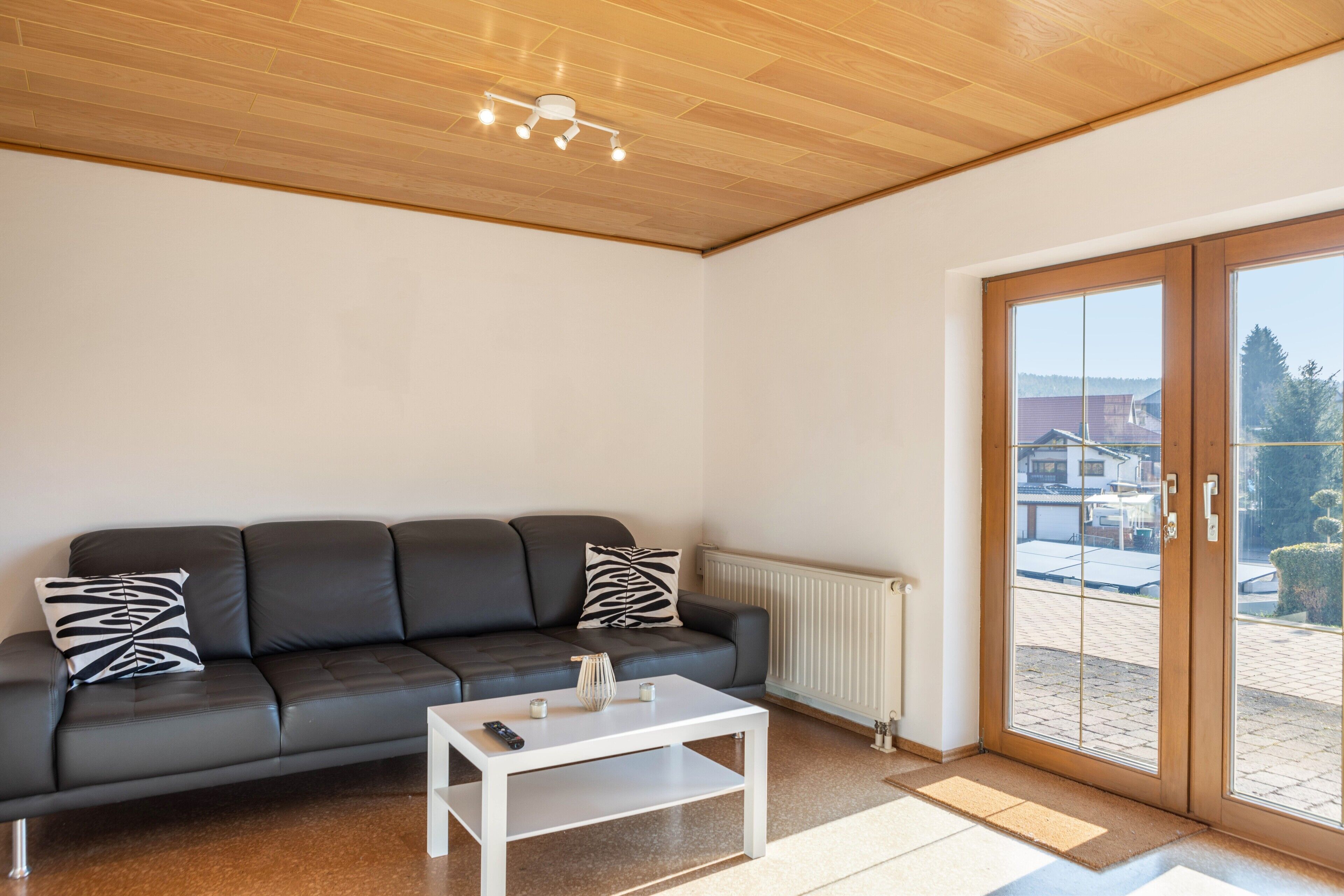 A modern living room with a black leather sofa, a white coffee table, and a sliding glass door leading to an outdoor area.