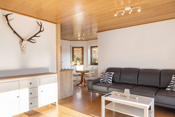 Un salón moderno con techo de madera, un sofá de cuero negro, una mesa de centro blanca y una calavera de ciervo montada en la pared.
