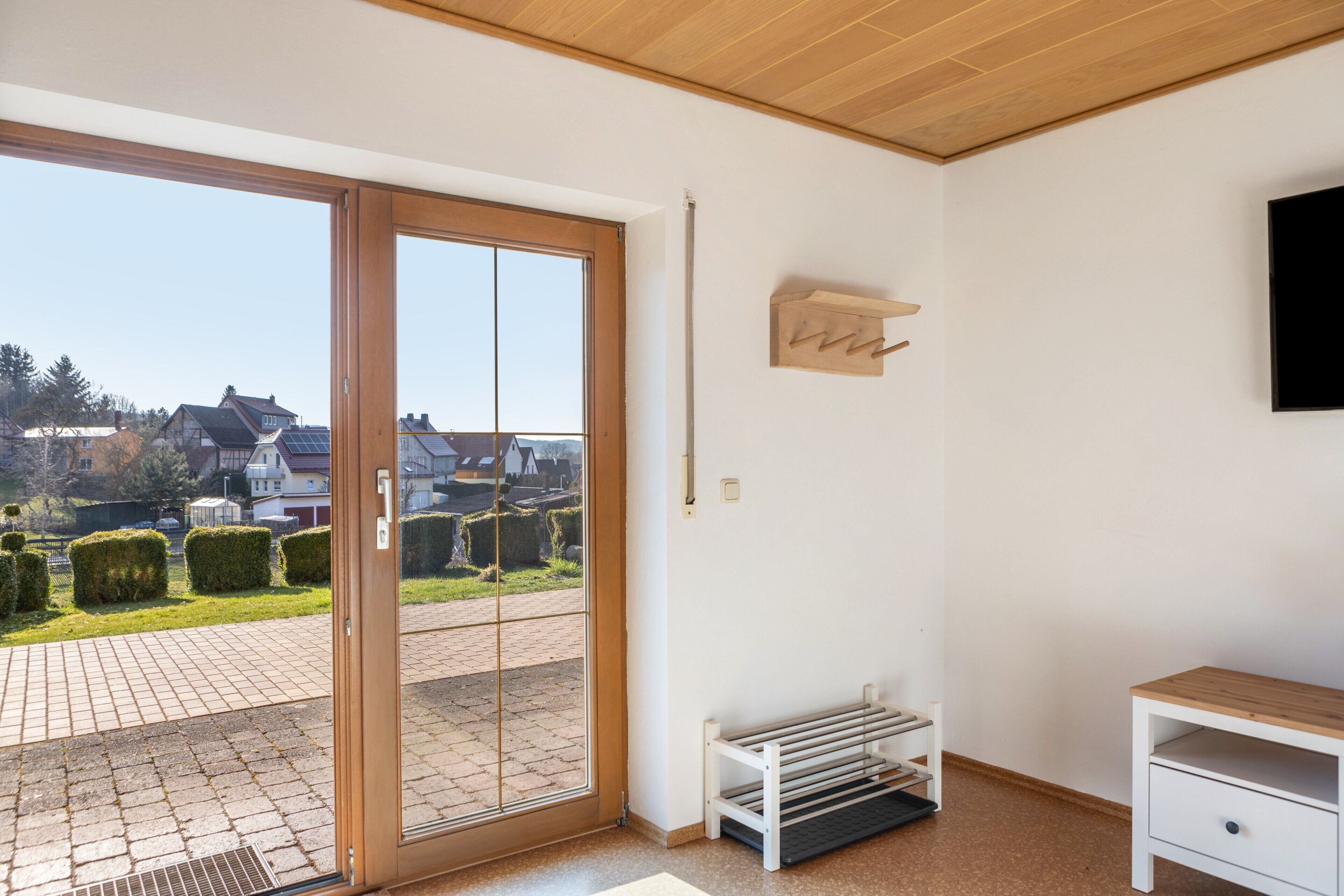 Ein Zimmer mit einer Schiebetür zum Patio, einer weißen Bank, einem kleinen Tisch und einem an der Wand befestigten Fernseher.