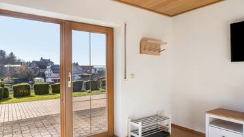 Ein Zimmer mit einer Schiebetür zum Patio, einer weißen Bank, einem kleinen Tisch und einem an der Wand befestigten Fernseher.