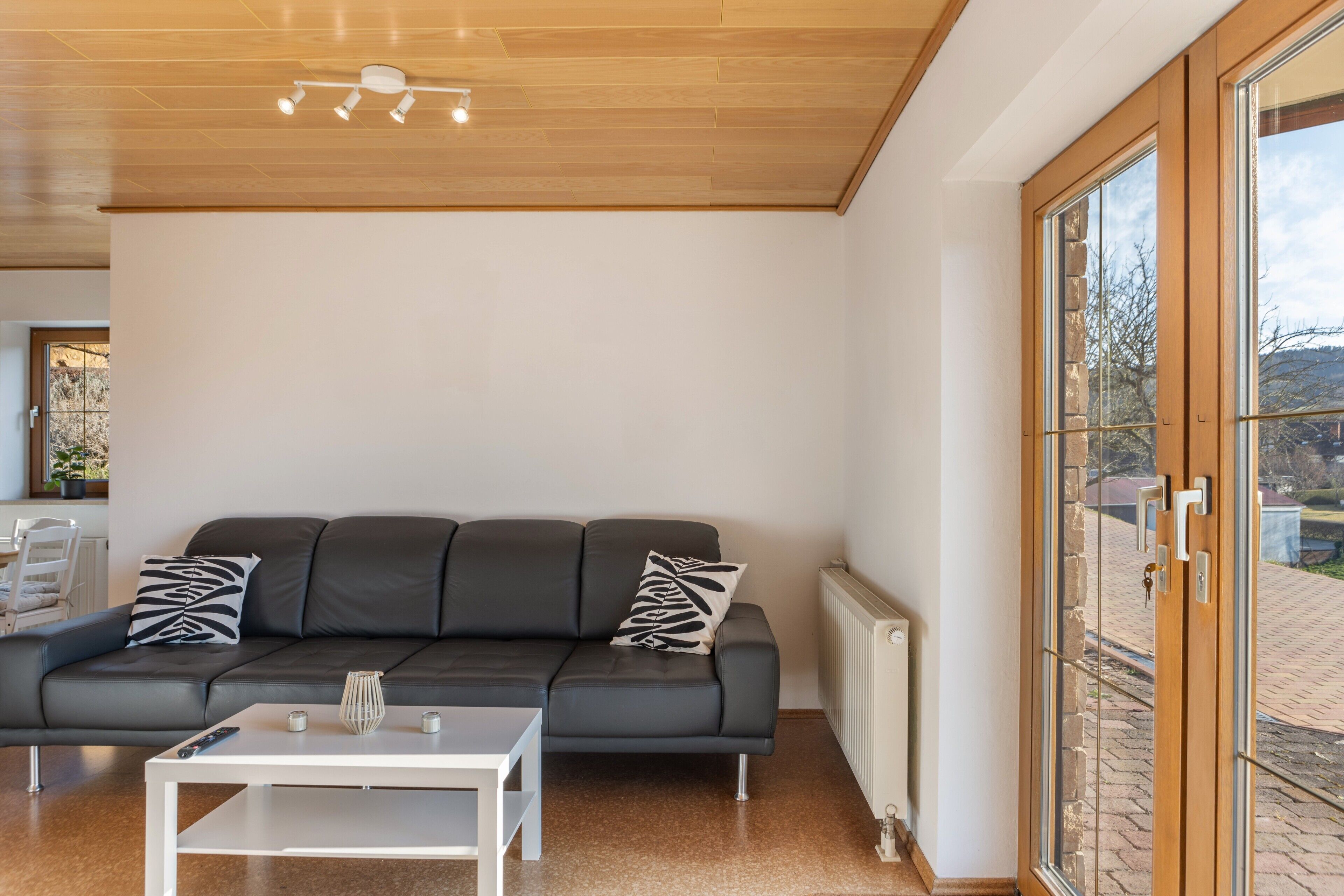 Een moderne woonkamer met een grijze bank, een witte salontafel en een groot raam met uitzicht op het omliggende landschap.
