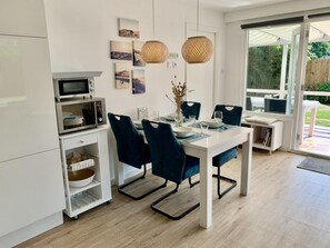 Una cocina moderna con armarios blancos, microondas integrado y comedor con mesa blanca y sillas azul oscuro.