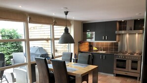 A modern kitchen with dark cabinets, stainless steel appliances, and a dining area with a table and chairs. - Equipped Bungalow, 5 Persons (Sint Maartensvlotbrug)