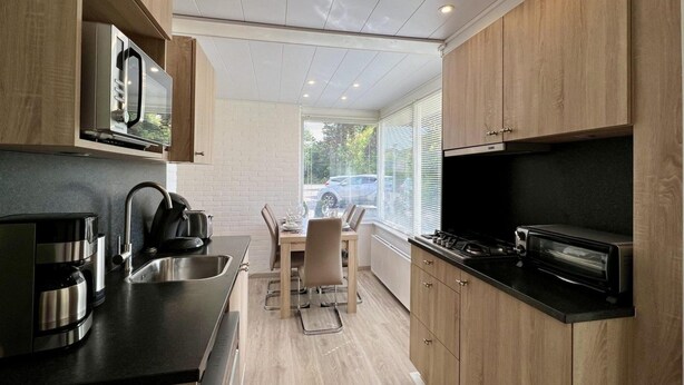 Una cocina moderna con armarios de madera, encimera negra, electrodomésticos de acero inoxidable y un comedor con mesa y sillas.