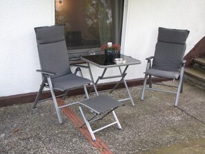 Eine Terrasse mit zwei Stühlen und einem Tisch, ein Fenster mit Blick und ein kleiner Blumentopf.