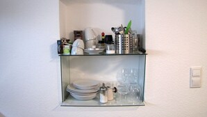 A kitchen with a glass shelf holding plates, cups, and a coffee maker.