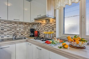 A modern kitchen with white cabinets, a tiled backsplash, a gas stove, and a window with frosted glass. - Apartment Jakara (Medulin)