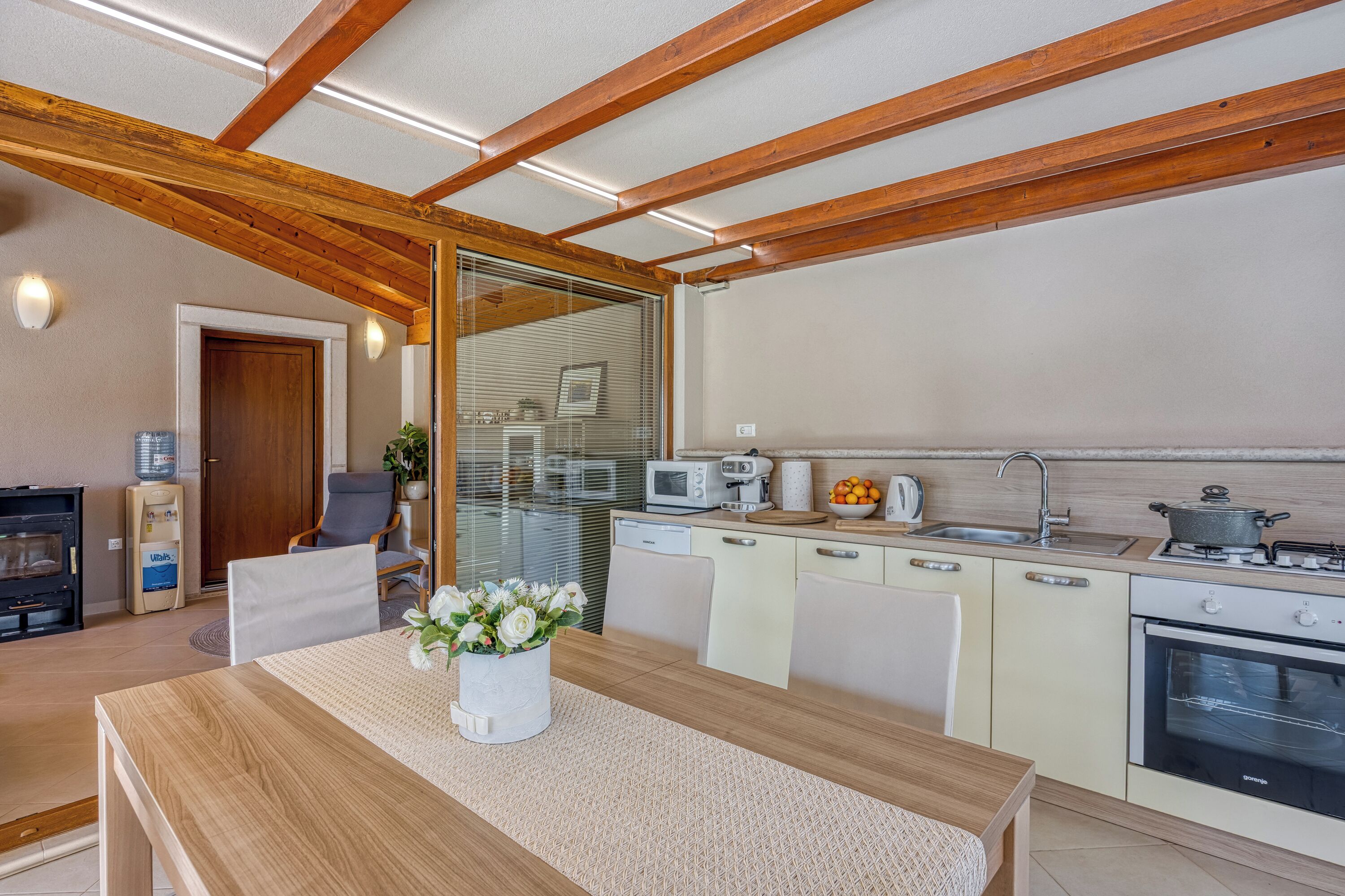 A modern kitchen with wooden beams, a dining area with a table and chairs, and a refrigerator.