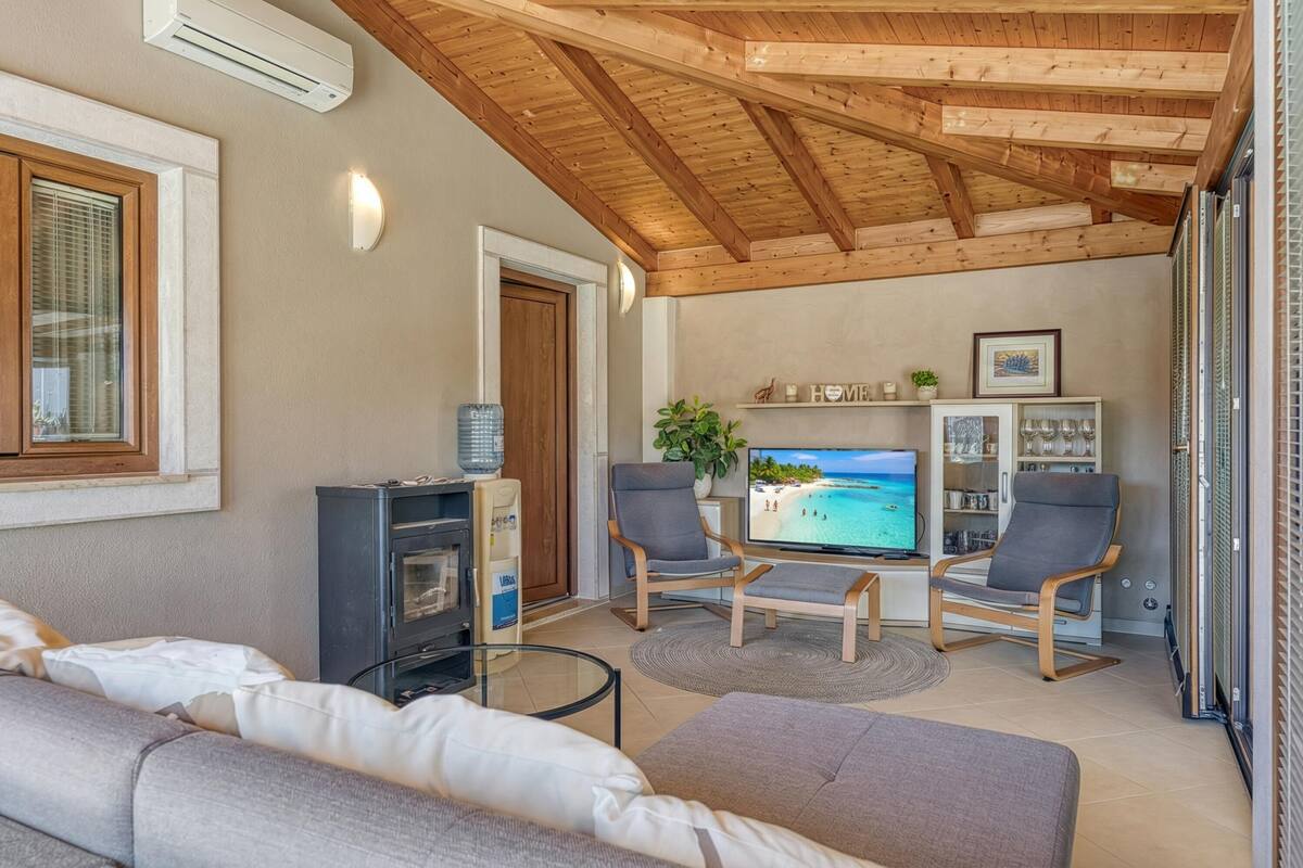A living room with a TV, two chairs, a sofa, a water dispenser, and a wooden ceiling.