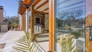 Una casa moderna con puerta de vidrio que da a una sala de estar, un patio con baldosas y plantas en macetas.