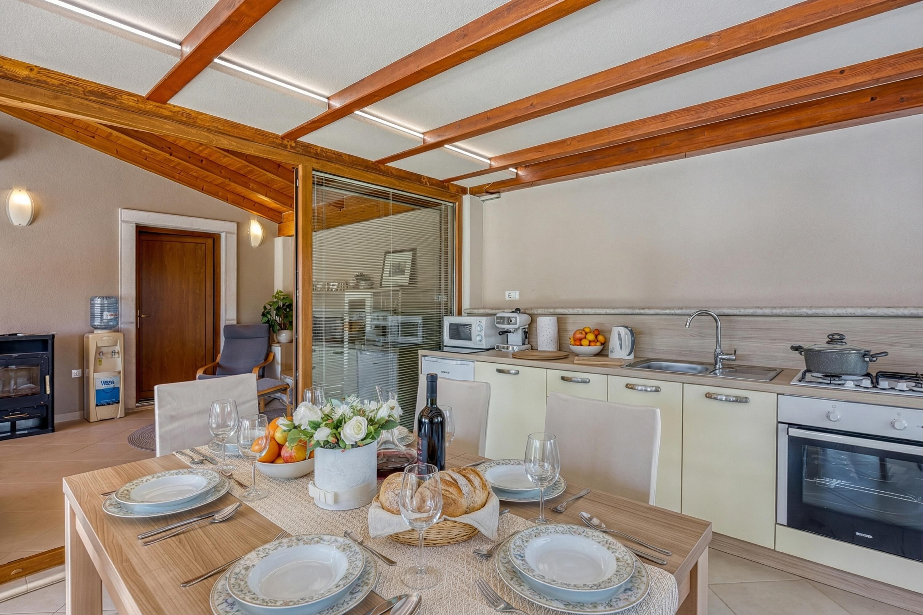 Una cocina moderna con vigas de madera, un comedor con una mesa dispuesta para cuatro personas, y vistas al salón.