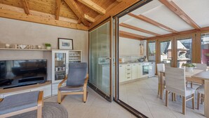 Una sala de estar moderna con un televisor de pantalla plana, vigas de madera en el techo, un sofá y una zona de comedor con una mesa y sillas.