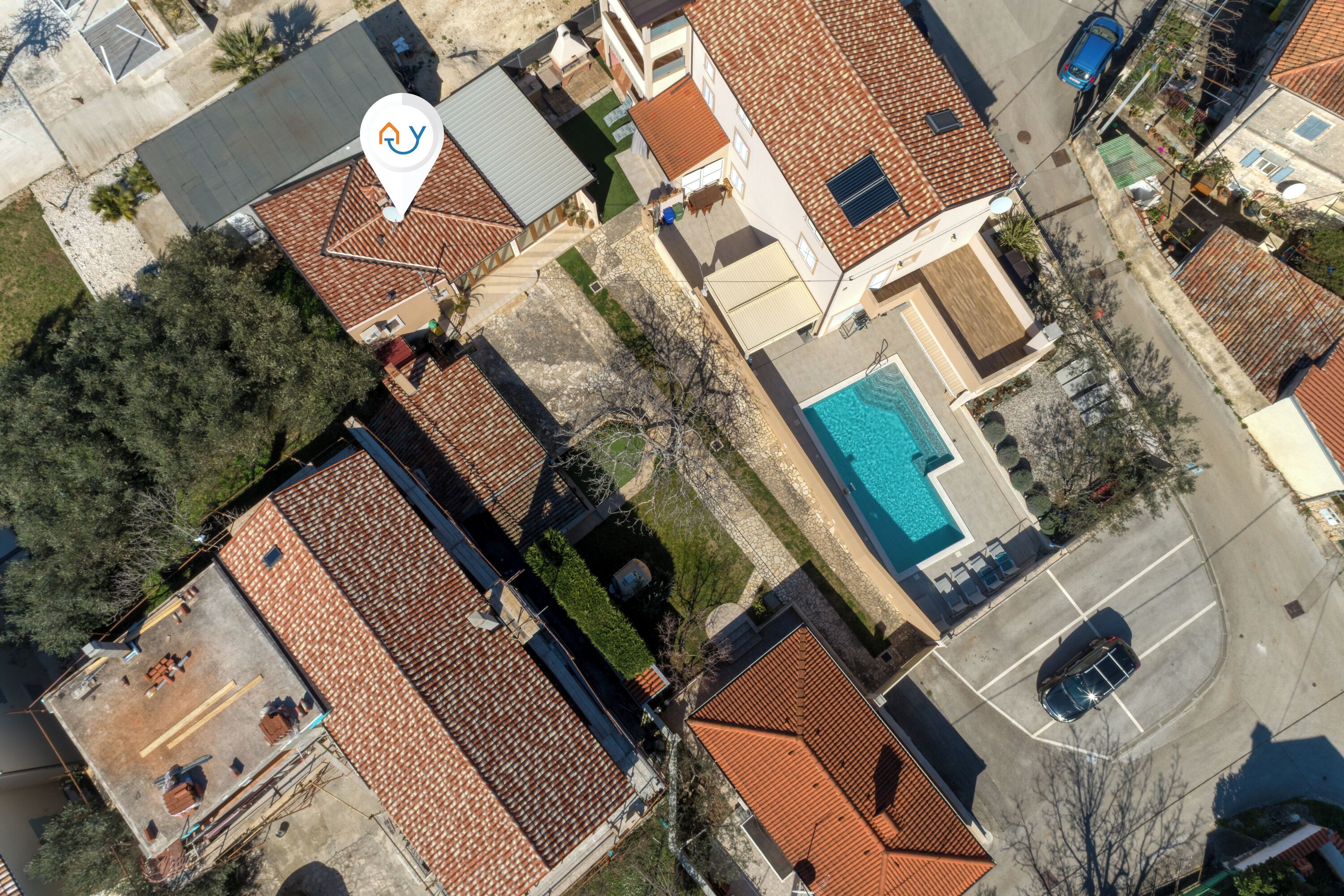 An aerial view of a residential area with multiple houses, a swimming pool, and a clear road.