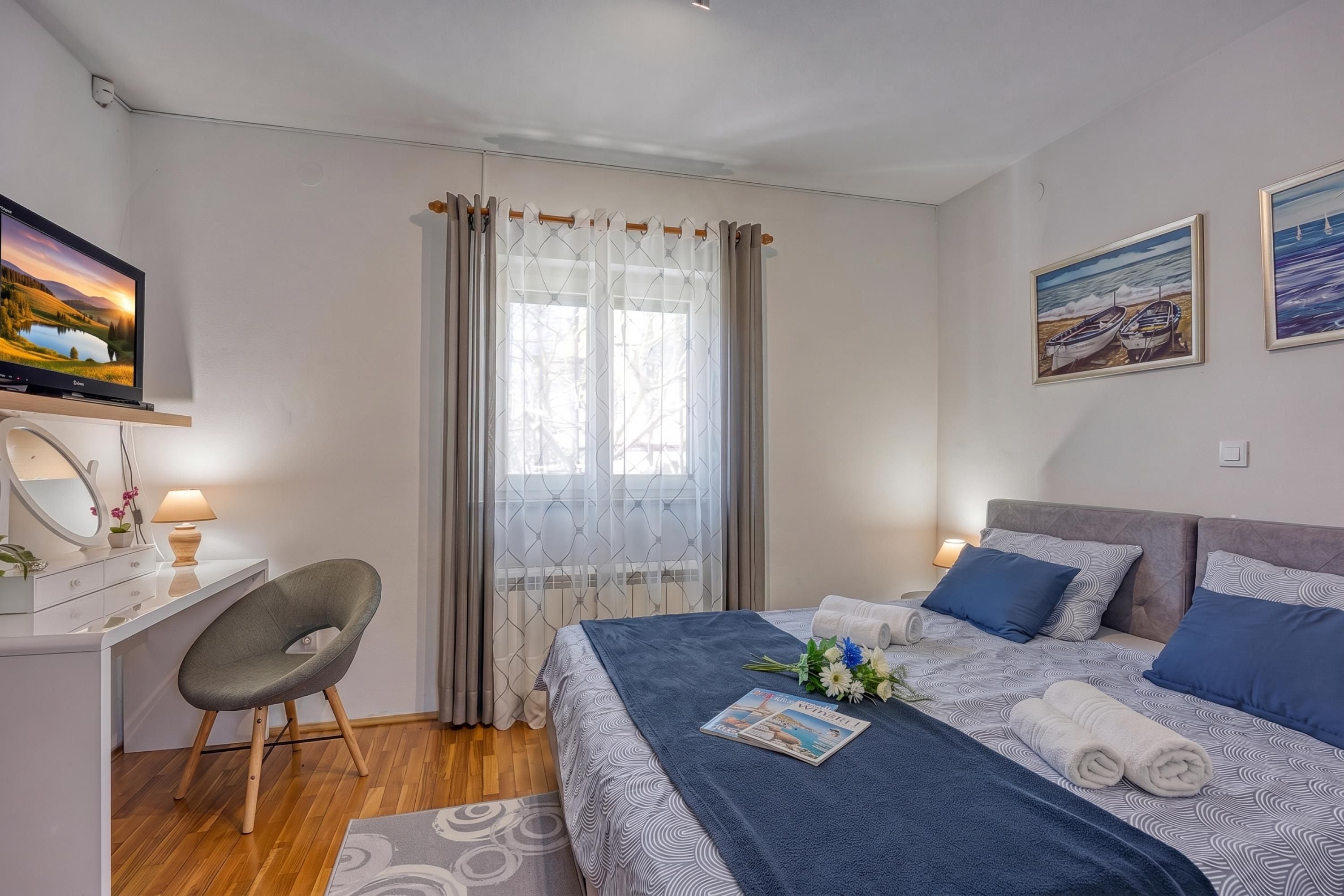 A bedroom with a bed, a desk, a chair, a television, and two paintings on the wall.