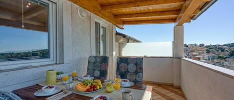 A balcony with a wooden ceiling, a table set with breakfast, and a view of the surrounding area.