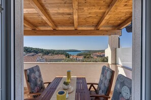 A wooden balcony with a table and chairs, overlooking a scenic view of a lake and surrounding hills. - Apartment Jakara 3 (Medulin)