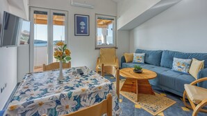 Una sala de estar moderna con un sofá, una mesa de comedor con mantel floreado y un televisor montado en la pared.