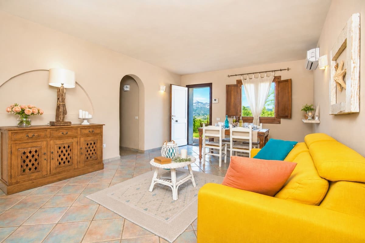 A living room with a yellow sofa, a wooden cabinet, and a dining area with a table and chairs.