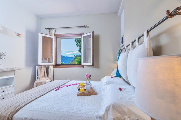 A bedroom with a bed, a window with curtains, a bedside table, and a tray with breakfast items. - Dimora Apartments (Arzachena)