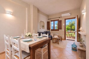 A dining area with a wooden table set for four, a sofa, and a view of the outdoors through a glass door. - Dimora Apartments (Arzachena)
