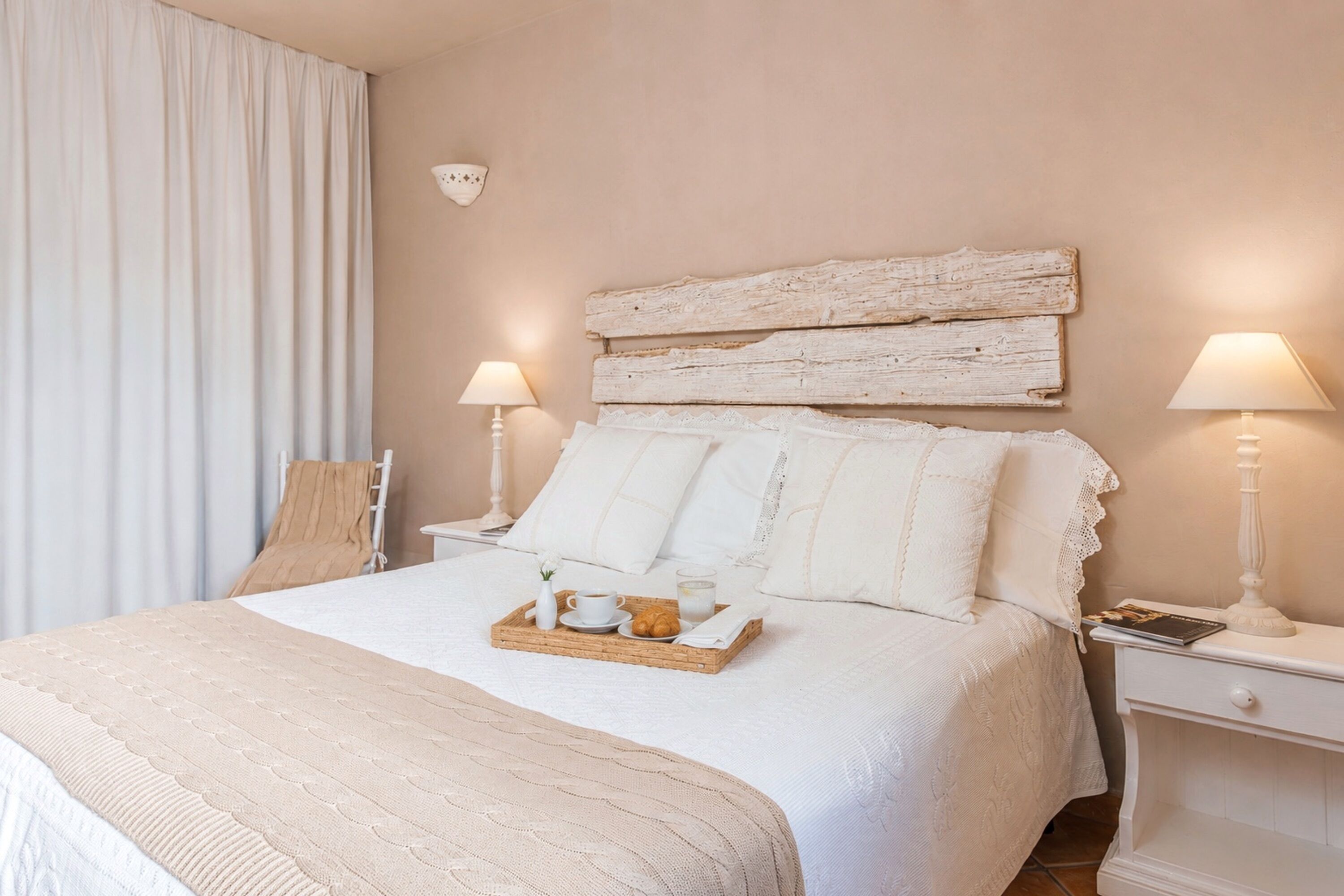 A neatly made bed with a tray of breakfast items, a bedside table with a lamp, and a rustic headboard.