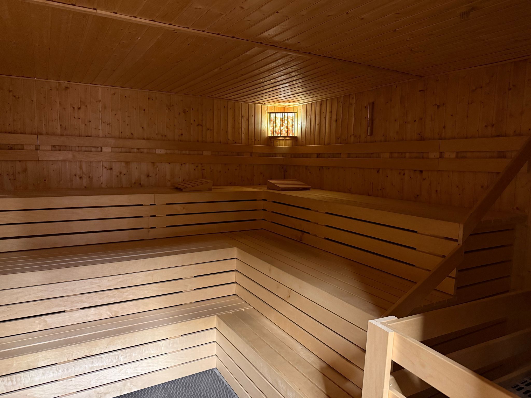 A sauna with wooden walls and benches, a central light fixture, and a sloped ceiling.