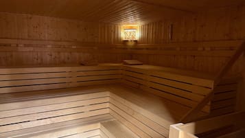 A sauna with wooden walls and benches, a central light fixture, and a sloped ceiling.