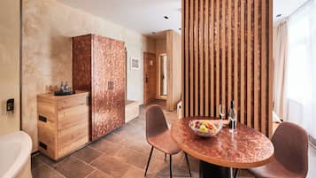 Una habitación de hotel moderna con un armario de madera, una mesa redonda con sillas, un frutero y una botella de vino.
