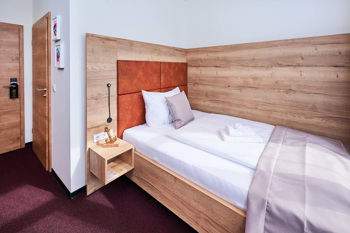 Una habitación de hotel con cabecera de madera, una mesita de noche con lámpara y una cama bien hecha.