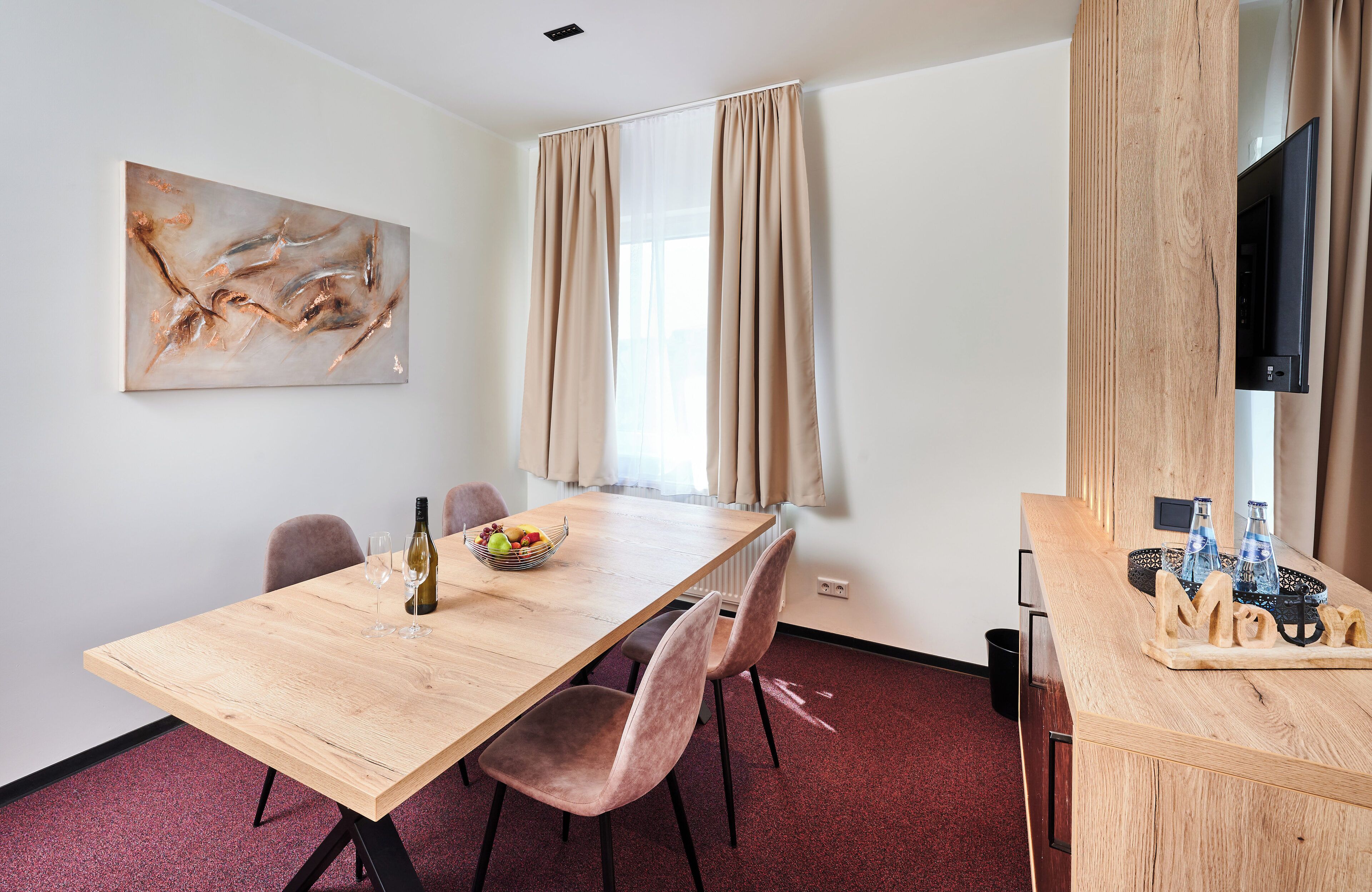 Una habitación moderna con una mesa de comedor de madera, sillas, un cuadro, un televisor y una pequeña zona de bar con botellas y vasos.