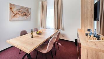 Una habitación moderna con una mesa de comedor de madera, sillas, un cuadro, un televisor y una pequeña zona de bar con botellas y vasos.