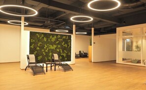 A modern office space with wooden flooring, circular ceiling lights, and a green leafy wall. There are two chairs and a small table. - Hotel 53 Nord (Brake)