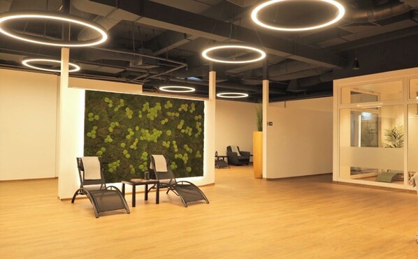 A modern office space with wooden flooring, circular ceiling lights, and a green leafy wall. There are two chairs and a small table. - Hotel 53 Nord (Brake)
