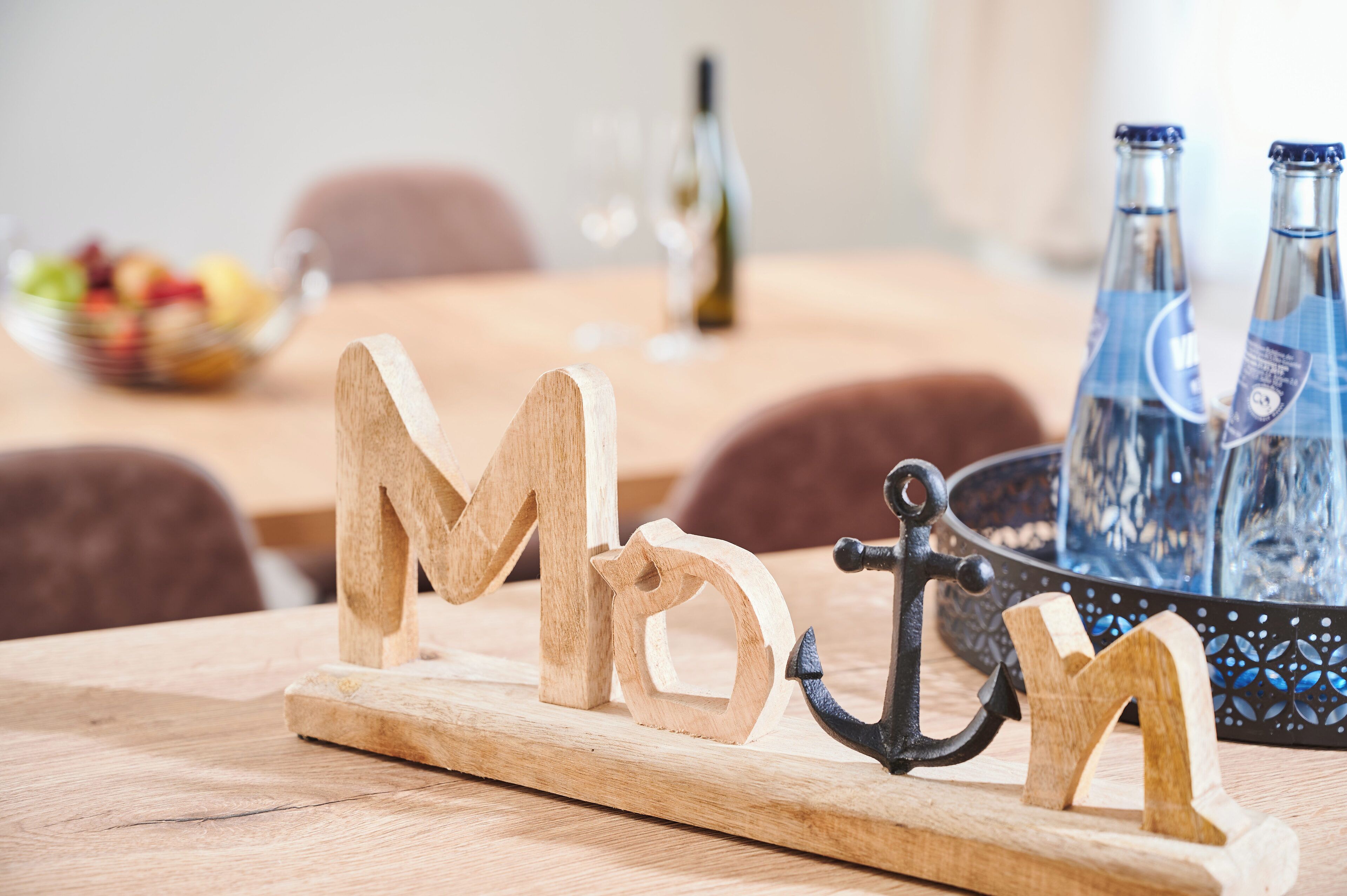 Wooden letters spelling "MD" on a wooden board, an anchor, and two bottles in a glass container on a table.