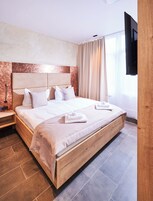 Uma cama grande com cabeceira de madeira, uma mesinha de cabeceira e uma televisão de tela plana na parede.