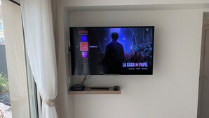 A television mounted on a wall displaying a movie titled "La Casa de Papel" with options for profile, visitors, and guests.
