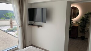 A bedroom with a bed, a TV mounted on the wall, a window with curtains, and a view of the outside.