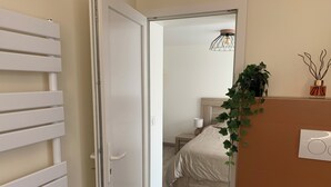 A bedroom with a bed, bedside table, lamp, and a hanging plant.