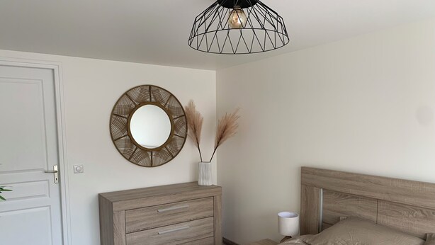 A bedroom with a wooden dresser, a round mirror, a bedside lamp, and a bed with a headboard.