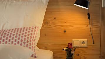 A neatly made bed with white and pink bedding, a bedside table with a vase of flowers, and a wall-mounted lamp.