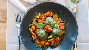 Un plato de comida con albóndigas, verduras y un tomate cherry sobre un plato oscuro.