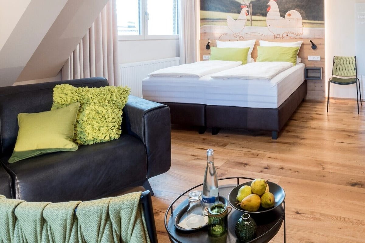 Un dormitorio moderno con cama, sofá y una mesa de comedor con fruta y una botella.