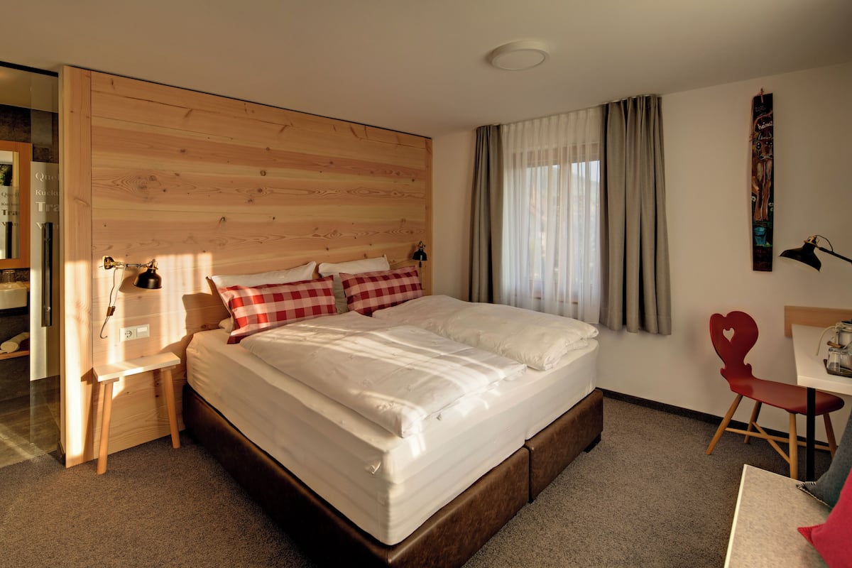 Un dormitorio con cabecera de madera, cama con ropa de cama blanca, escritorio con silla y una silla en forma de corazón rojo.