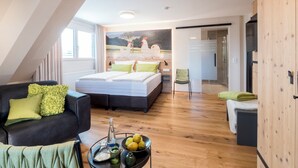 Un dormitorio moderno con una cama grande, una zona de estar con un sofá y una mesa de comedor con fruta y una botella.