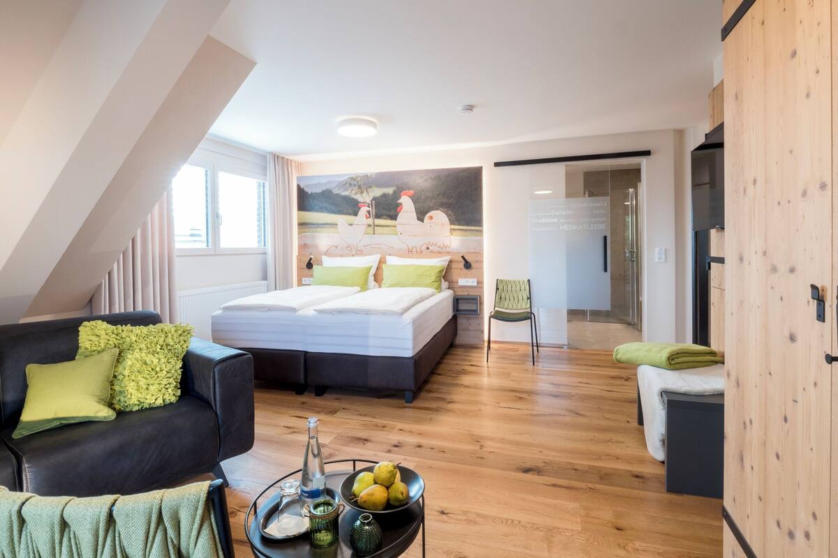 Un dormitorio moderno con una cama grande, una zona de estar con un sofá y una mesa de comedor con fruta y una botella.
